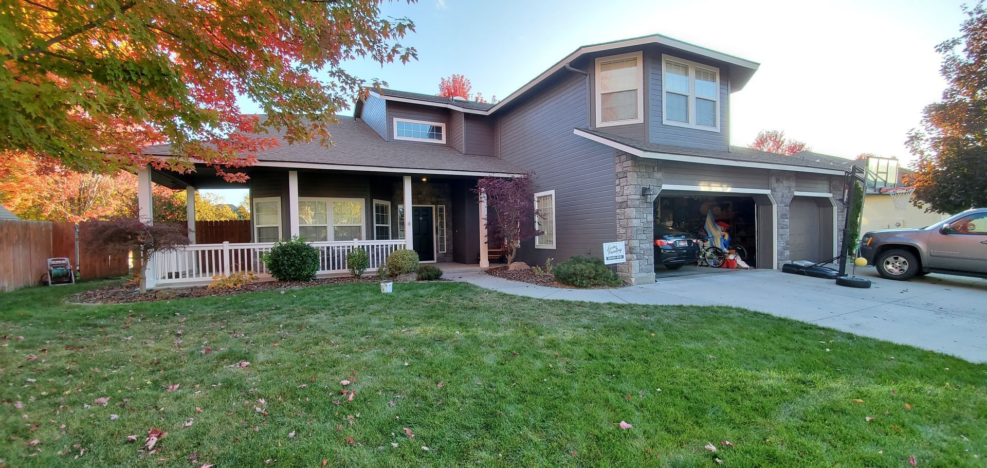 House with dark siding, a covered porch, and a two-car garage. Autumn foliage frames the home.