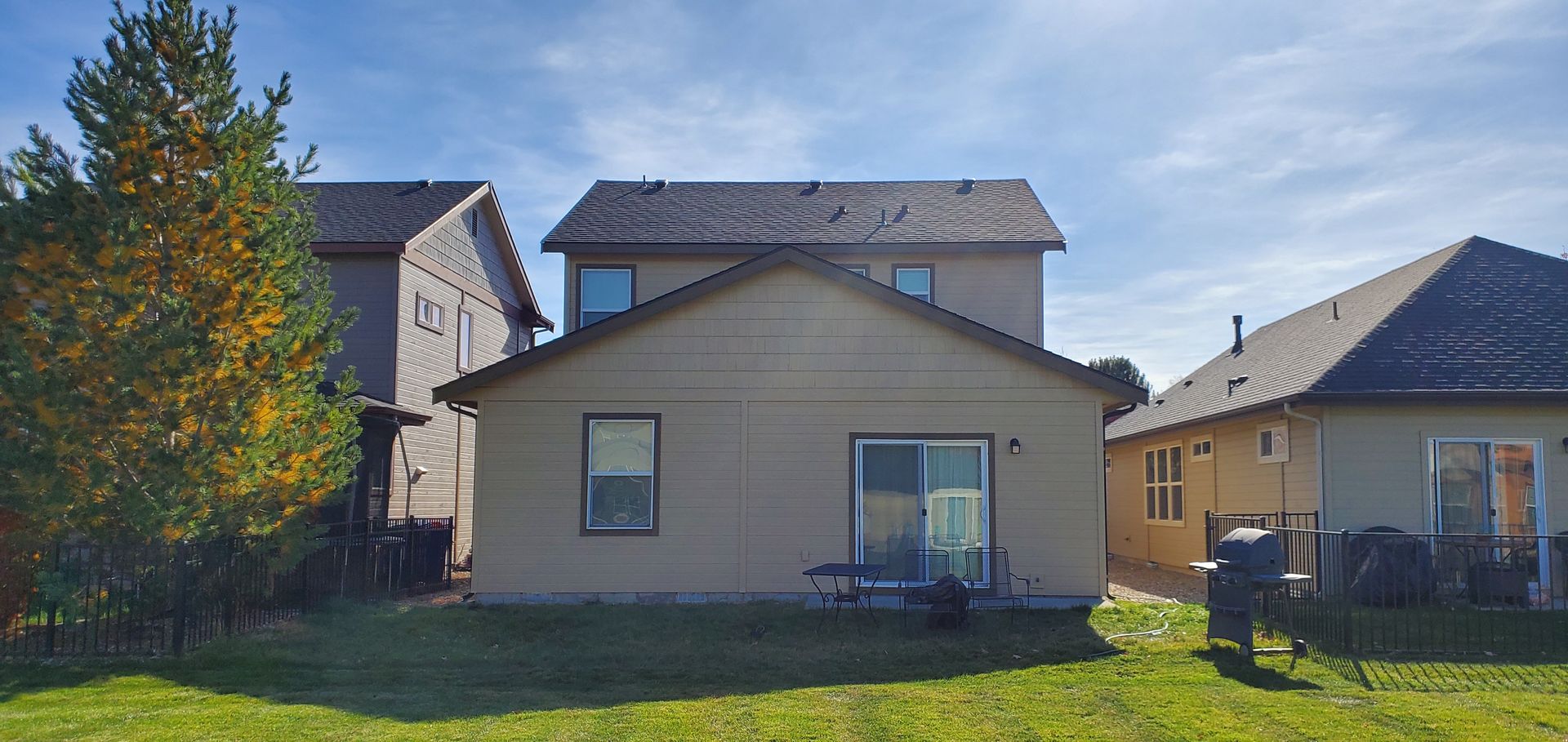 Backyard view of three houses on a sunny day. A tree is on the left. The houses are tan and have dark roofs.