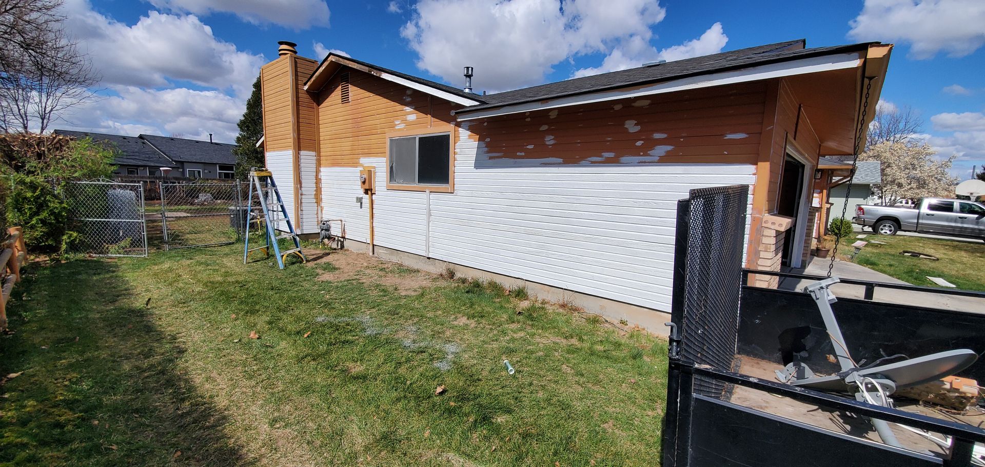 House exterior under renovation; white siding, brown framing exposed, green grass lawn, blue sky.