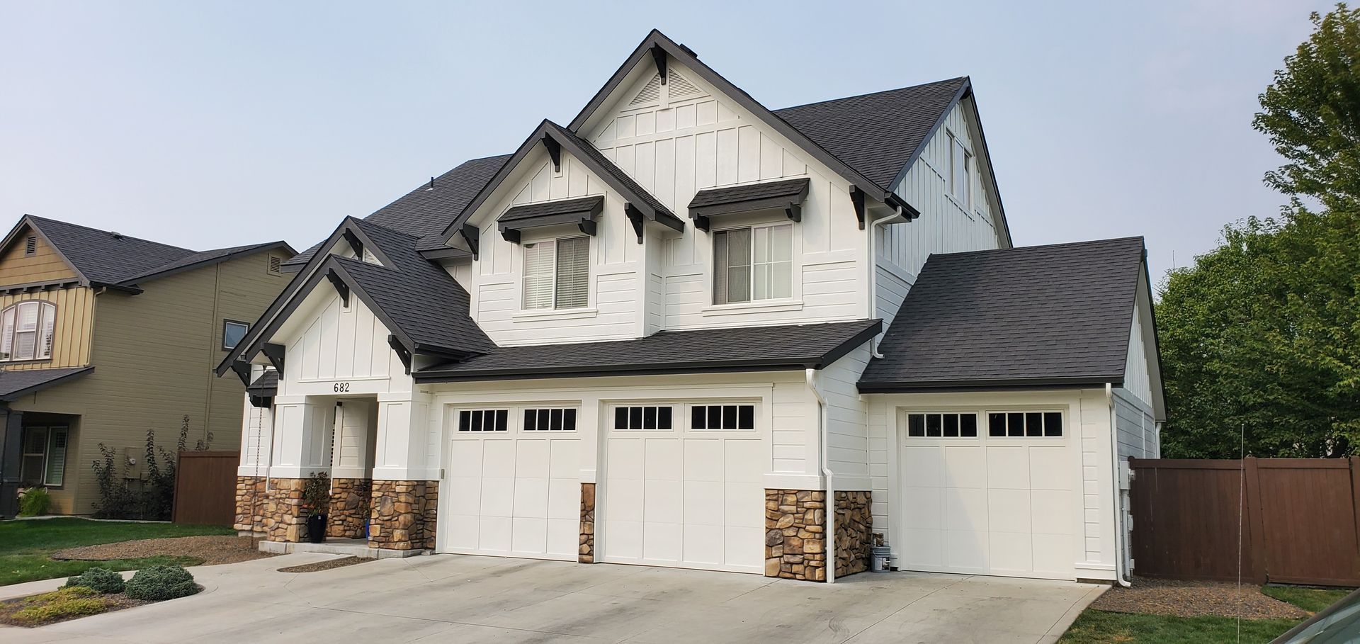 A white, modern two-story house with a dark roof and stone accents, set against a cloudy sky.