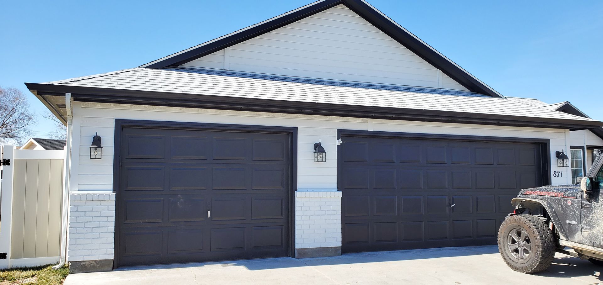 A two-car garage with a black roof and dark gray doors; a muddy Jeep sits to the right.