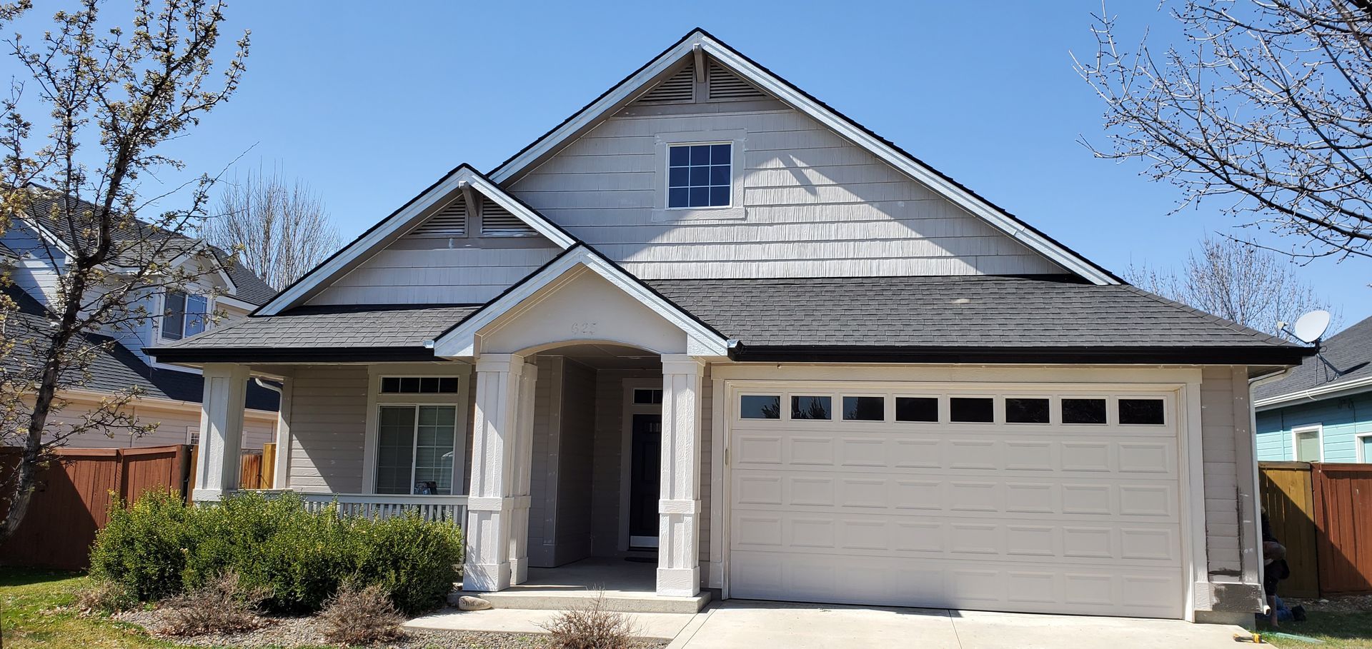A weathered two-story house with a garage, covered porch, and a small, square window on a sunny day.