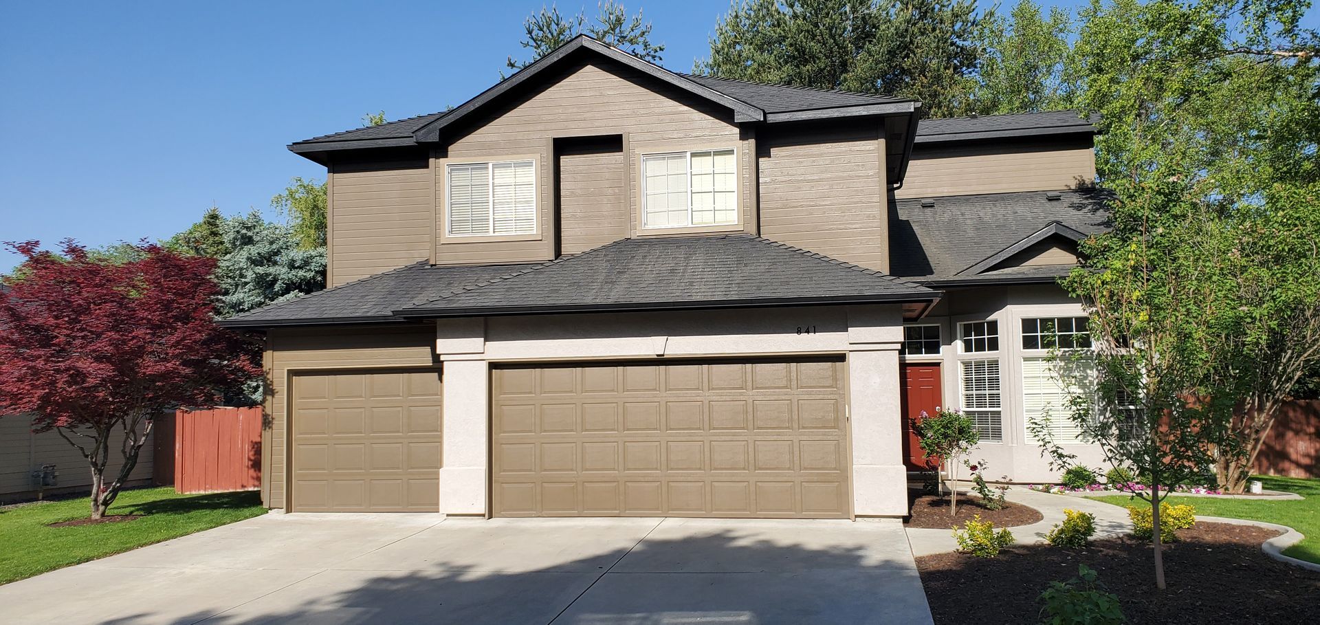 Two-story house with a brown garage door, a red front door, and a red tree on the left.