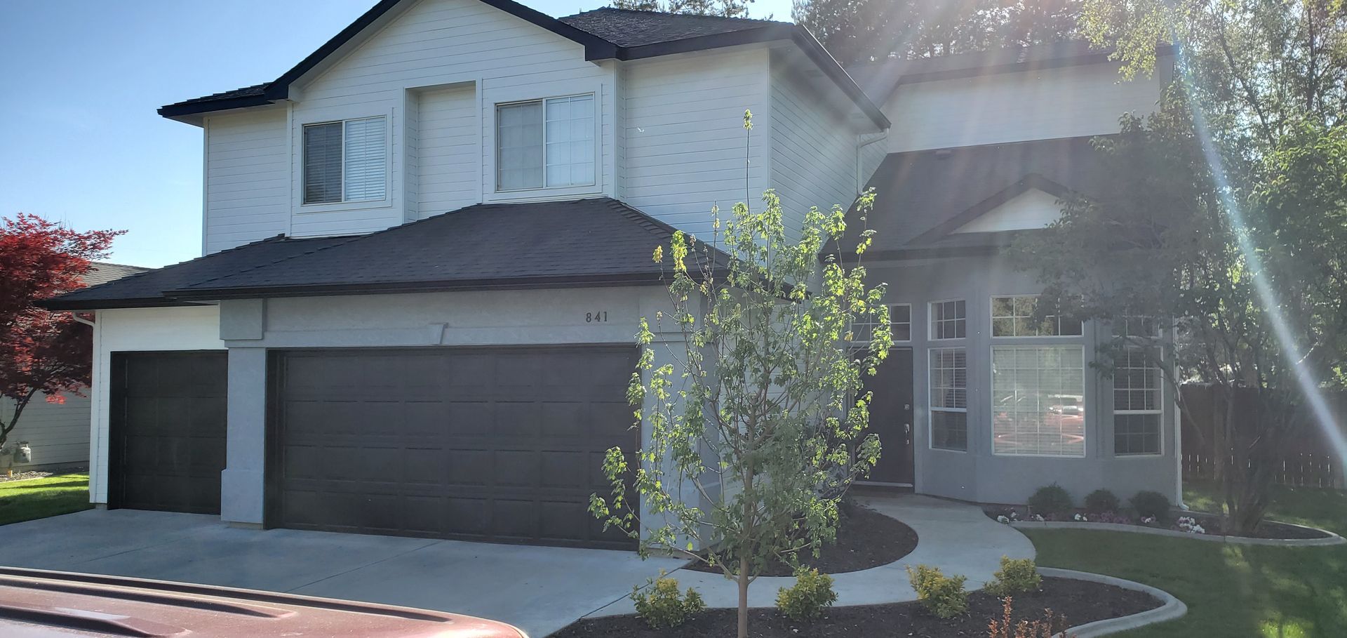 A two-story white house with a dark roof and two-car garage has a stone pathway leading to the front door, framed by trees.