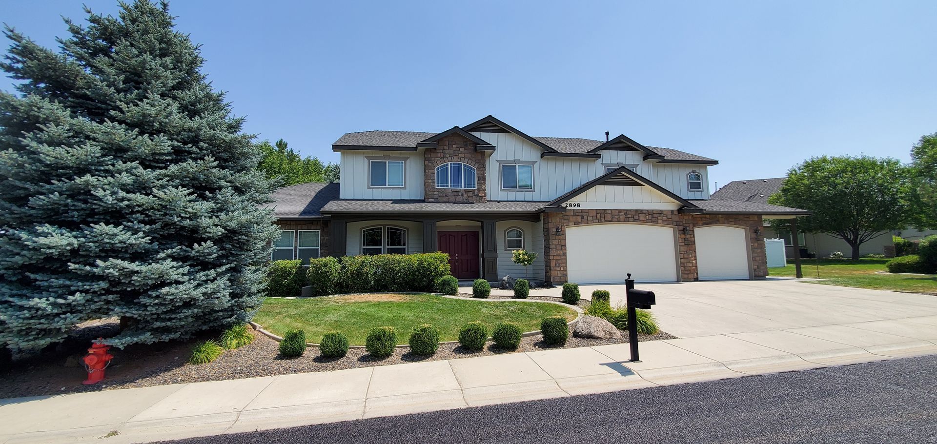A two-story house with a light-colored exterior, stone accents, and a two-car garage. It has a neatly landscaped front yard and a mailbox.