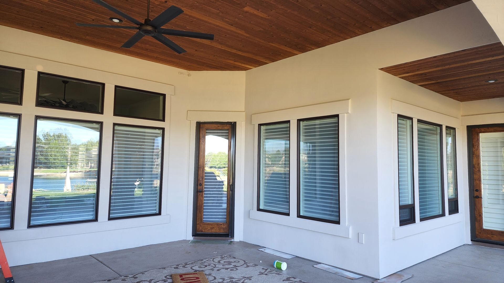 A covered patio with a wooden ceiling, white walls, and large black-framed windows and doors.