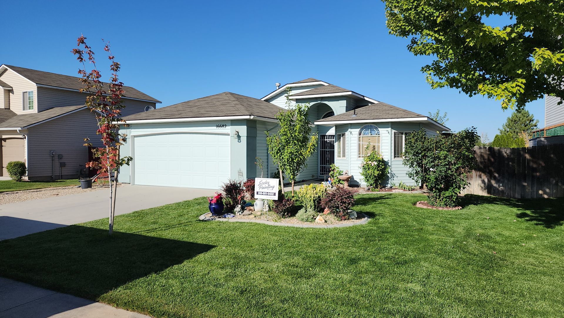 A light blue house with a two-car garage and well-manicured lawn under a clear blue sky.