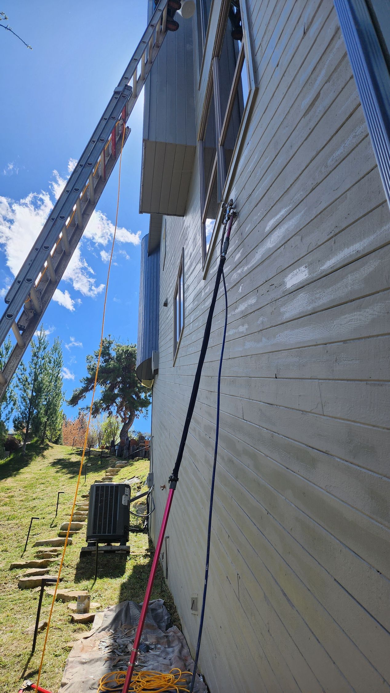 A large box is being lifted by a crane up the side of a building. A ladder is also propped against the building.