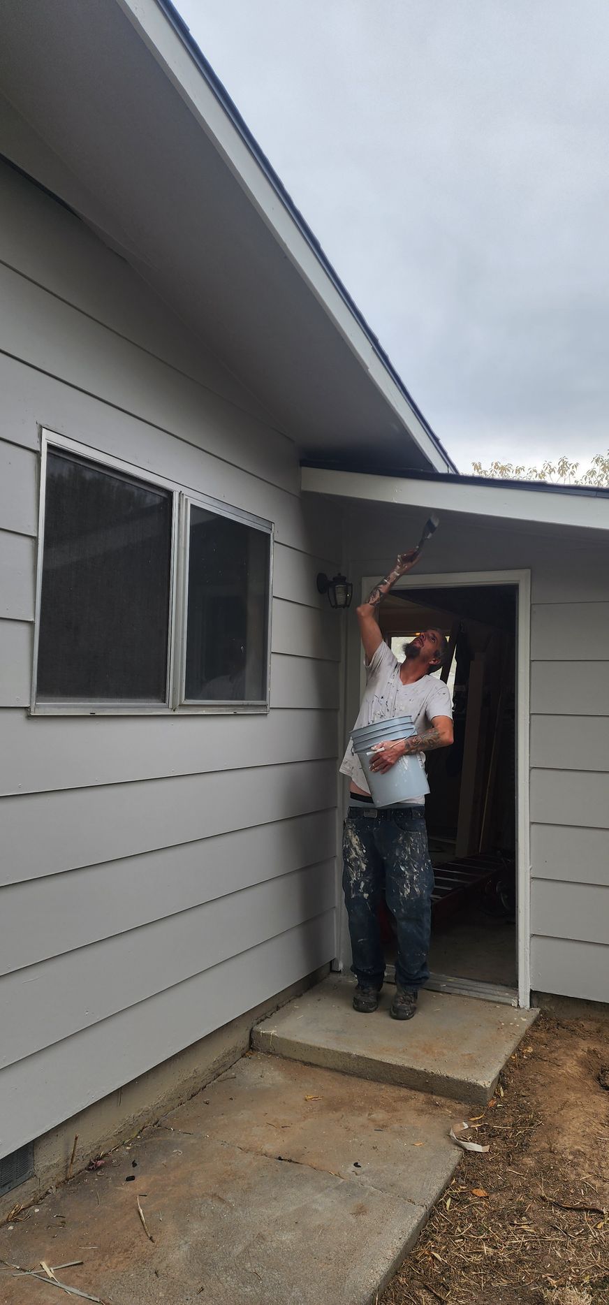 A person painting the exterior of a house. They are standing in a doorway and reaching up to paint under the eaves.