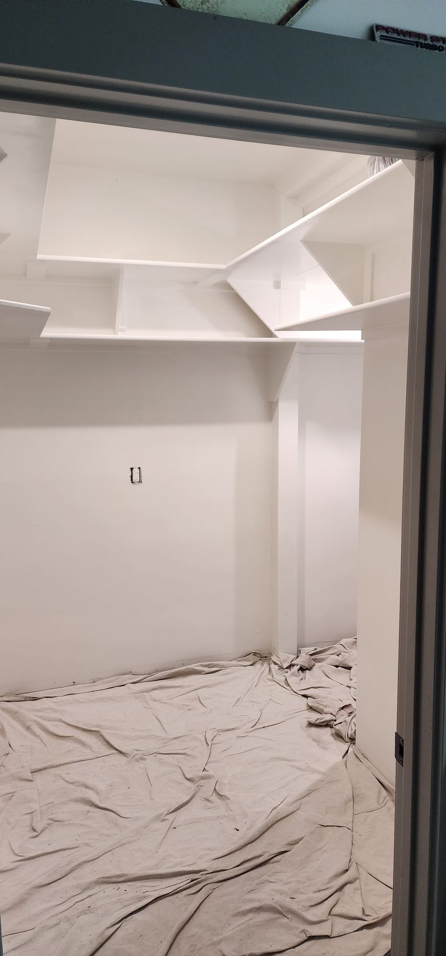 An empty white room with a textured ceiling and drop cloths covering the floor, viewed through an open door.