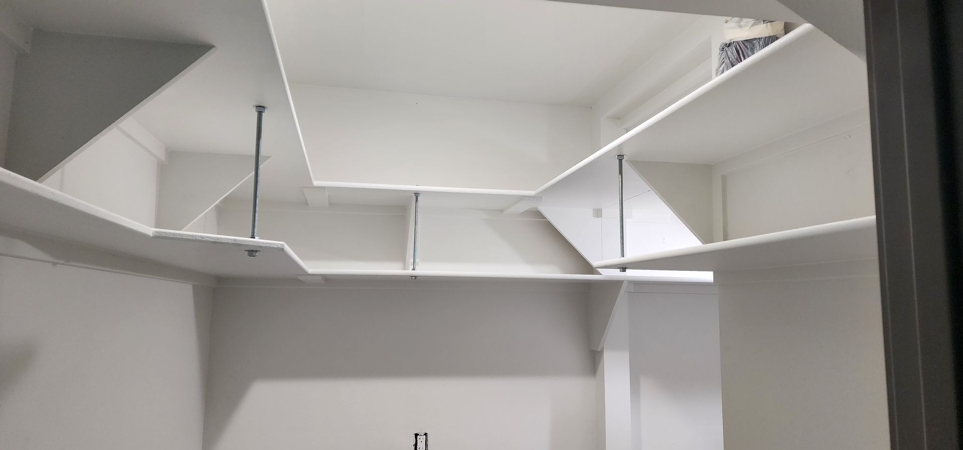 White closet with built-in shelving, including angled and straight shelves, supported by metal rods. The closet walls are white.