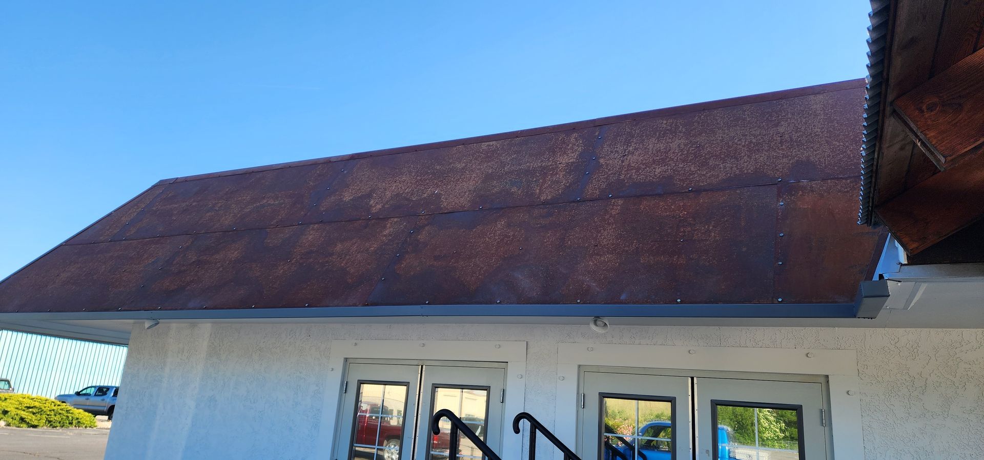 View of a white building with a brown, weathered roof, against a clear blue sky. The building has several windows.