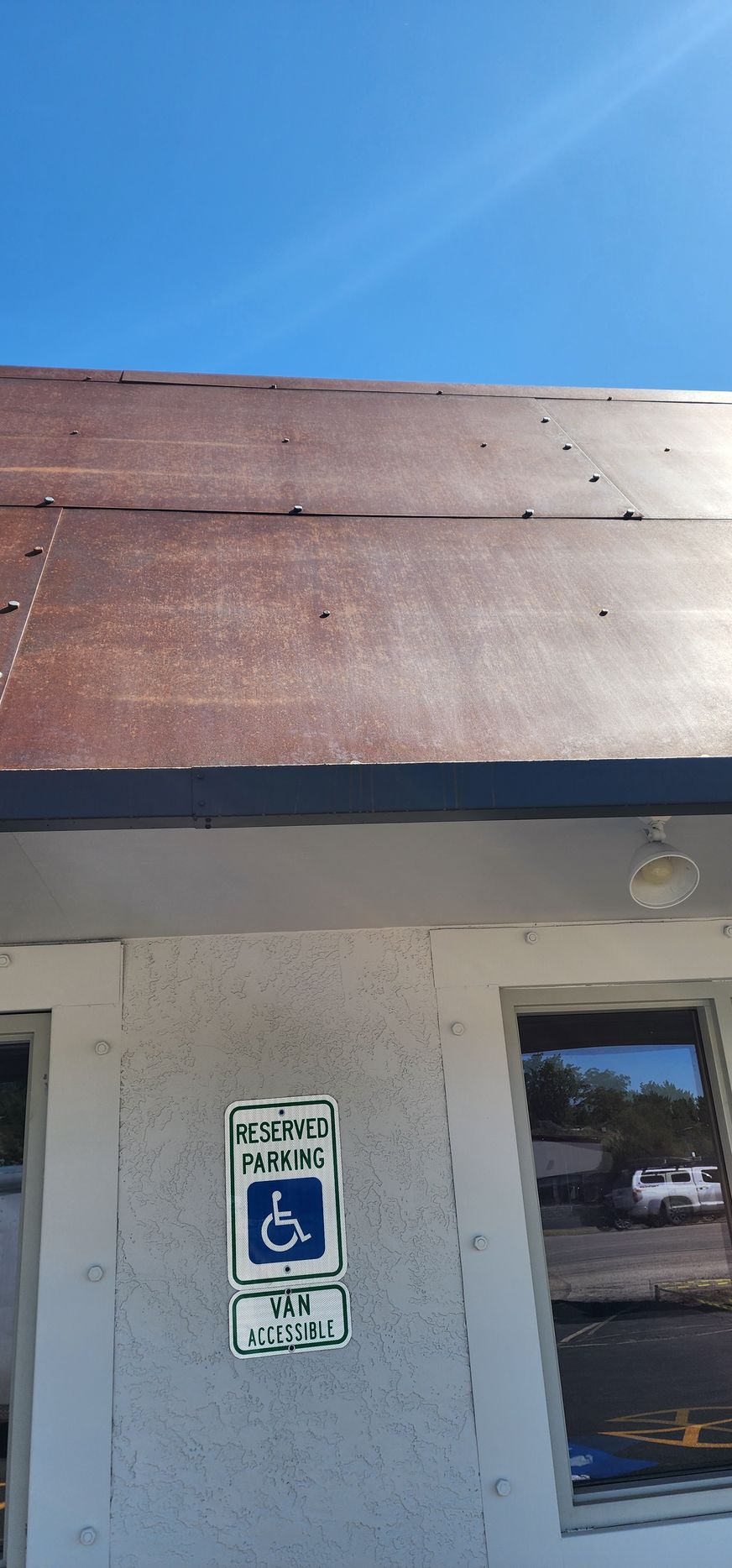 Building with a rusted metal roof and a handicapped parking sign on the wall; clear blue sky in the background.