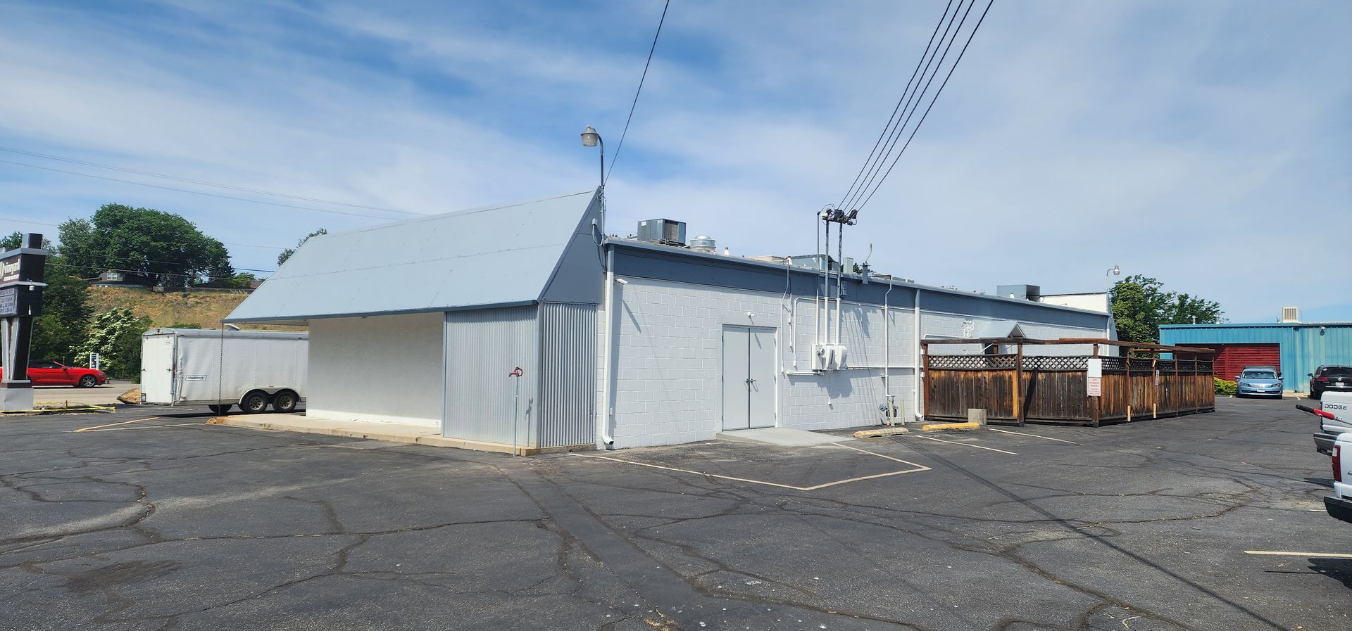 A gray building with a slanted roof sits under a blue sky. It appears to be a commercial building, possibly a restaurant, with a parking lot in front.