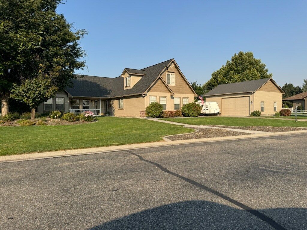 A house with tan stucco siding and a detached garage, on a green lawn. Blue sky.