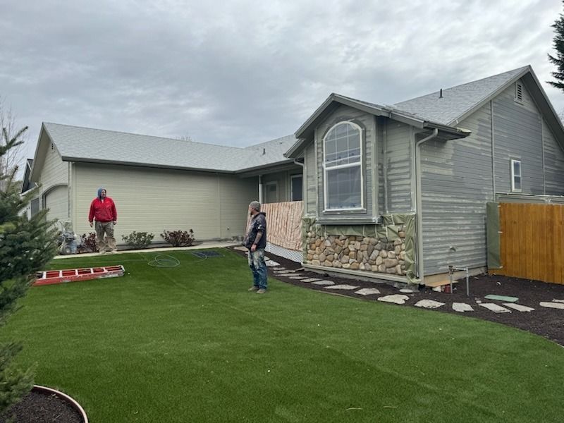 A man is standing in front of a house with a ladder in the backyard.