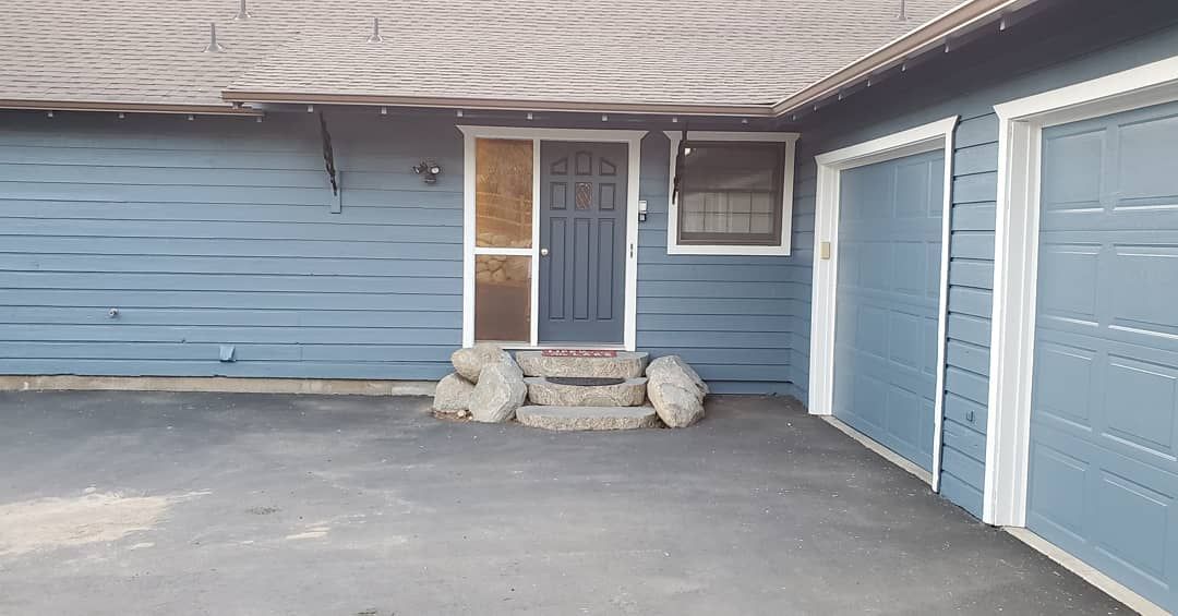 Blue house with a dark blue front door, steps, and two garage doors on a gray asphalt driveway.