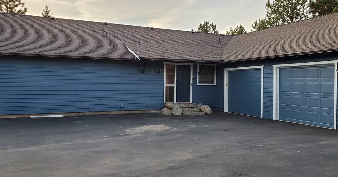 Blue house with two garage doors and a front door, surrounded by a black asphalt driveway.