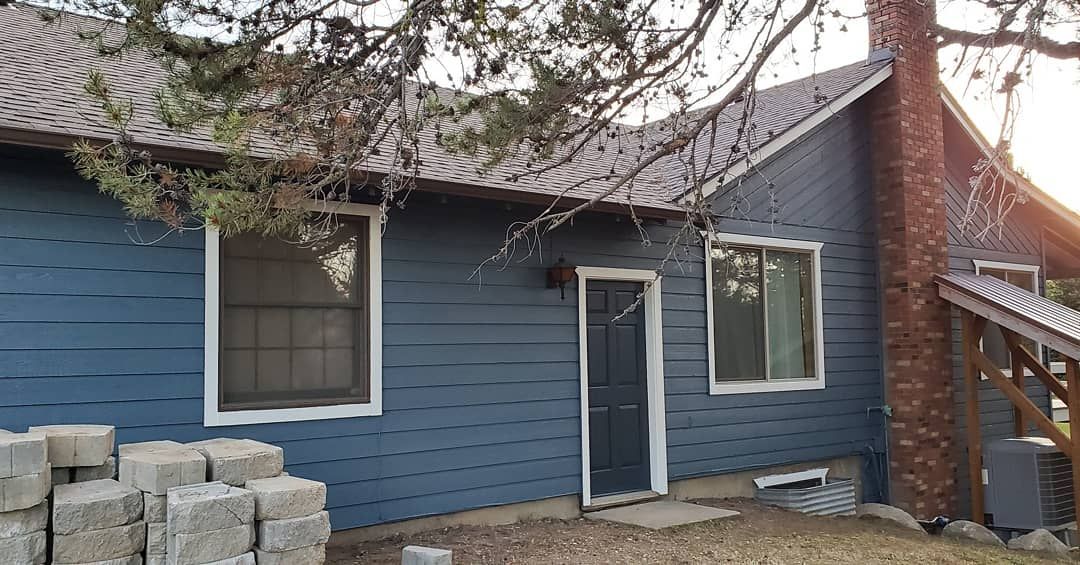 Blue-sided house with a brick chimney, front door, and windows. Grey cinder blocks sit in the foreground.