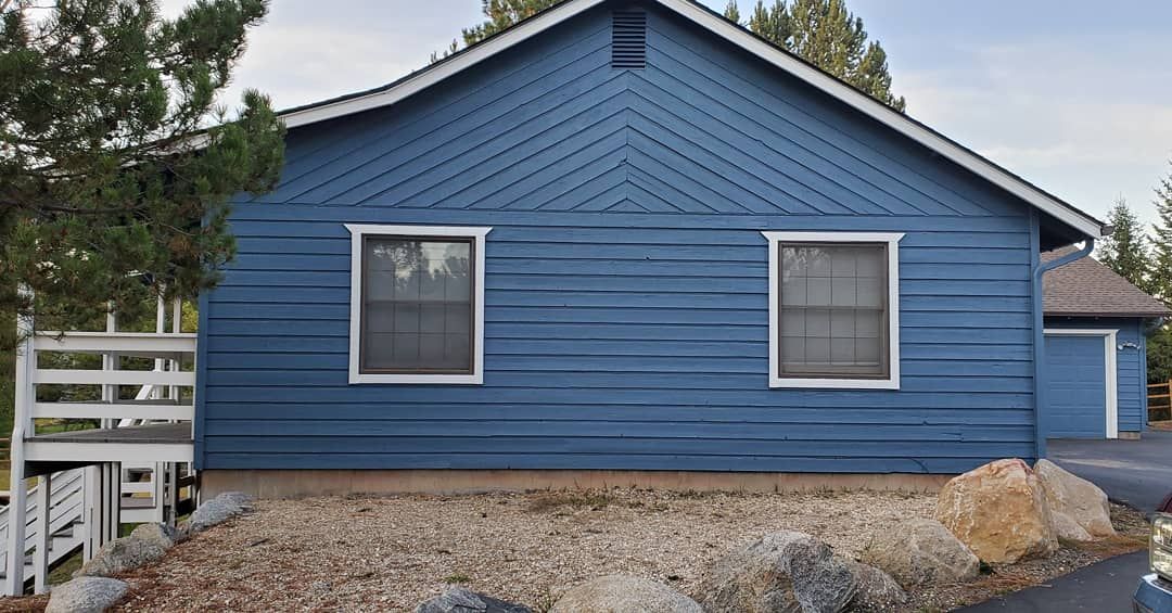 Blue-painted house with two windows, gravel landscaping, and a small deck.