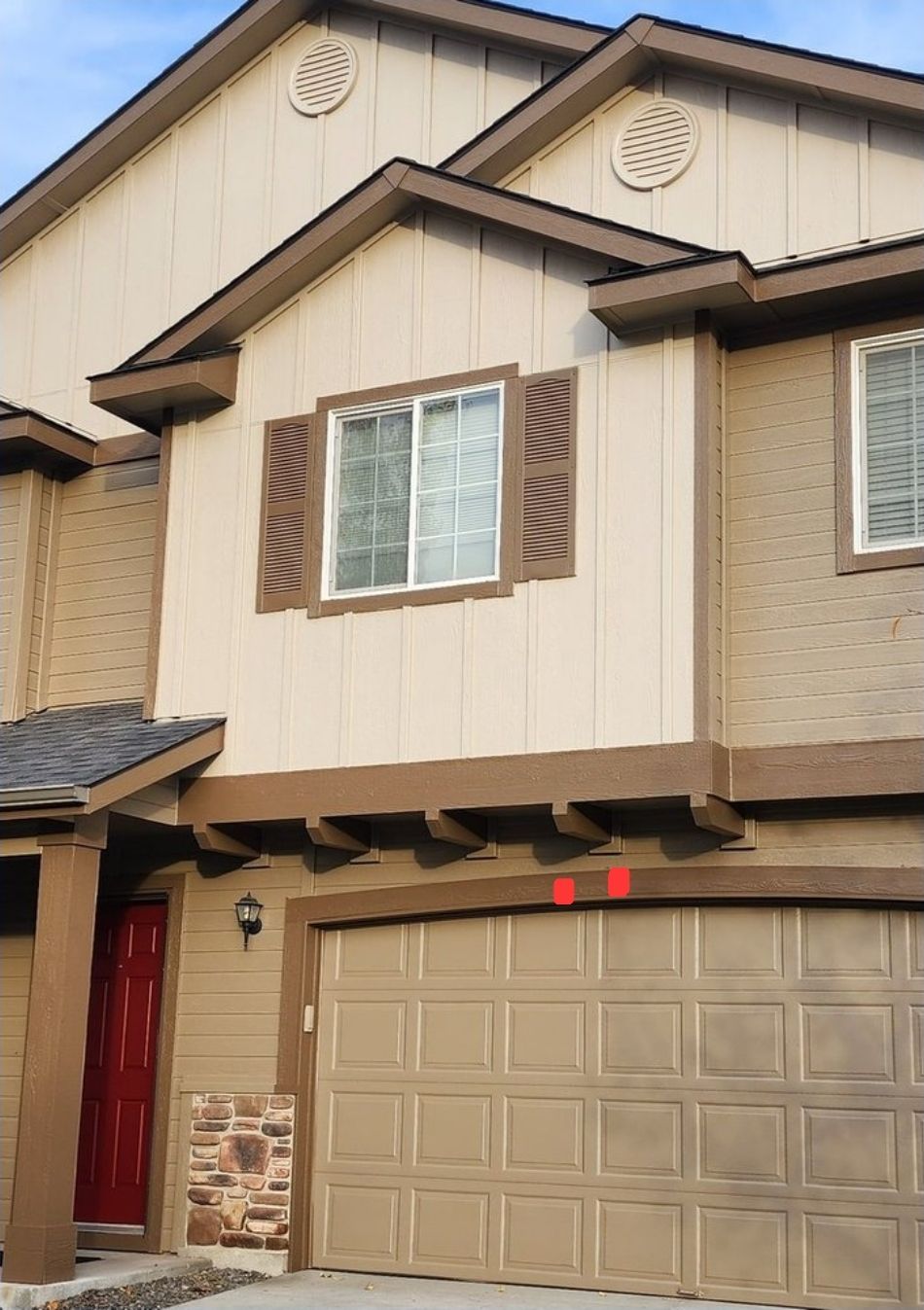Two-story townhouse with a tan garage door, brown shutters, and a red front door.