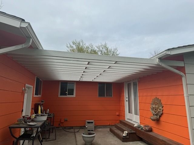 A house with orange siding and a white pergola on the patio.
