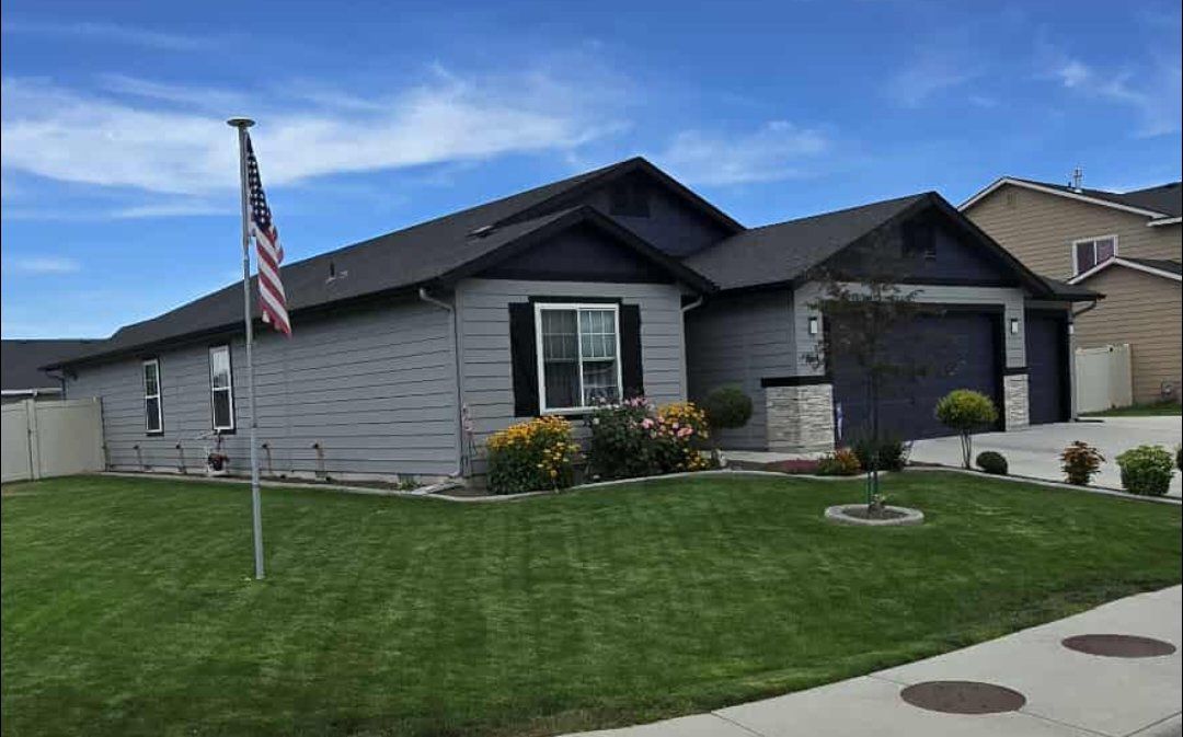 Gray house with blue trim, American flag in yard, green lawn, blue sky.