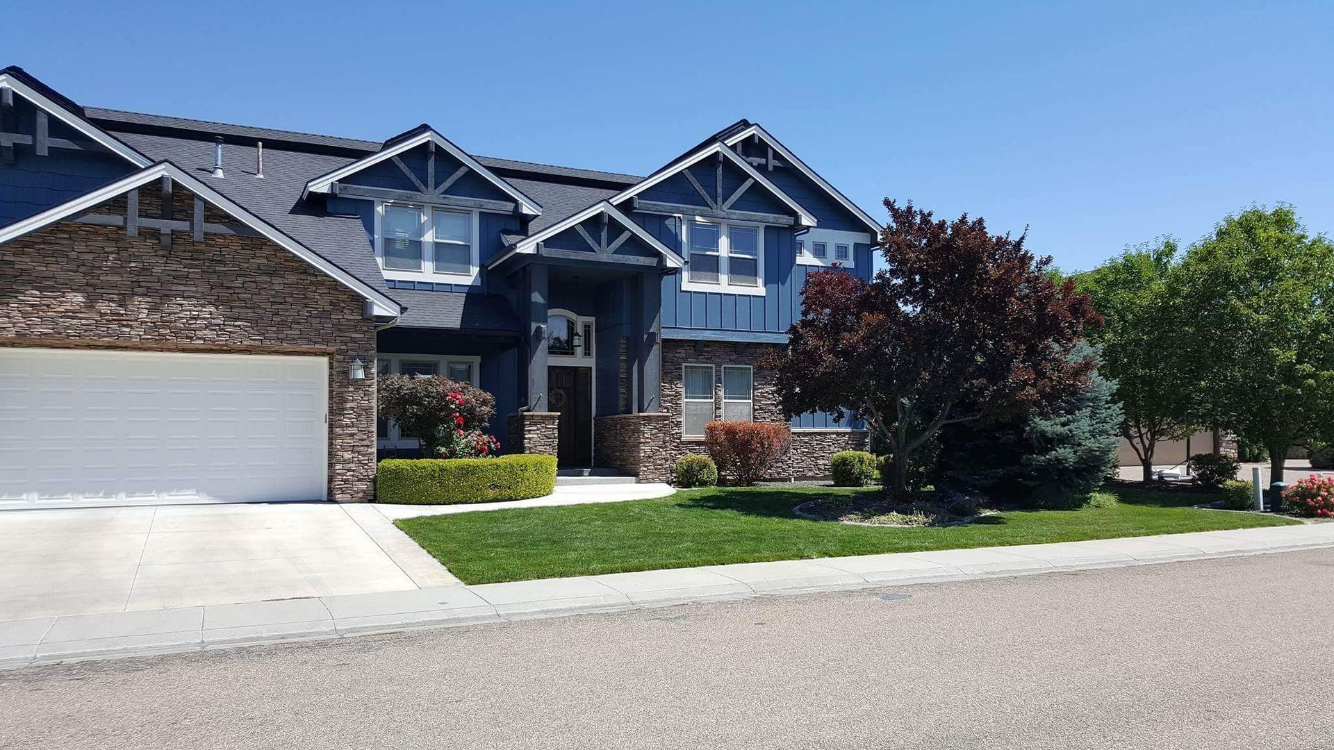 Blue and stone two-story house with a garage and well-manicured lawn on a sunny day.
