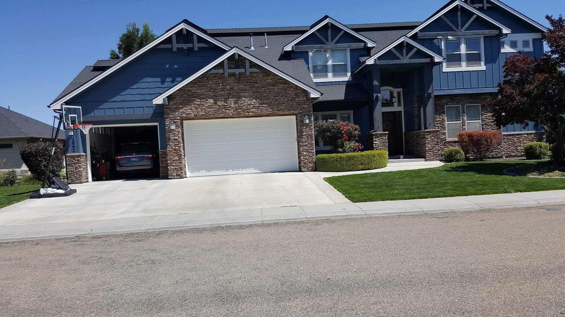 Two-story blue house with stone accents, a white garage door, and a driveway, under a clear blue sky.