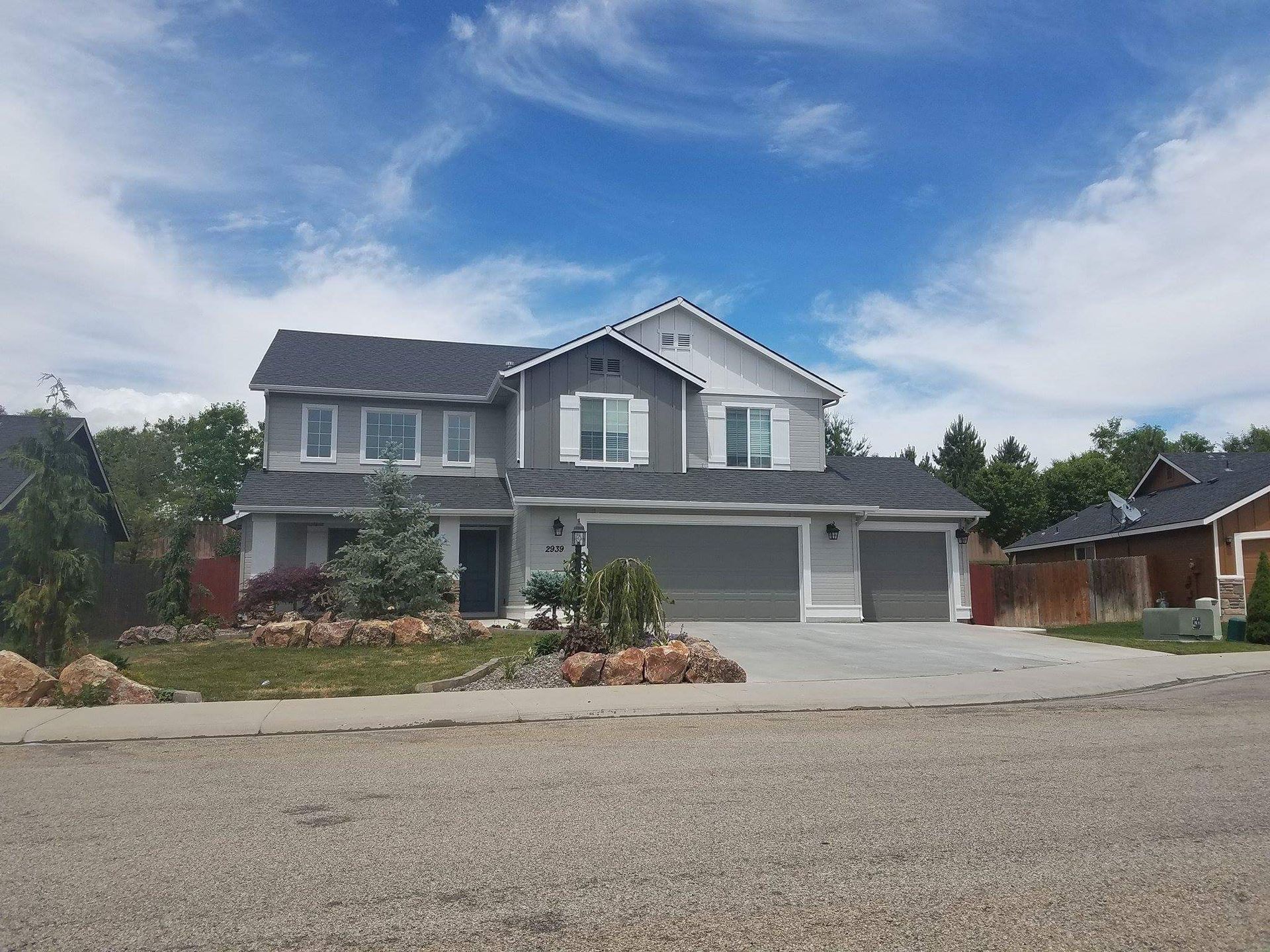 Two-story gray house with a three-car garage under a blue sky. Landscaping in front.