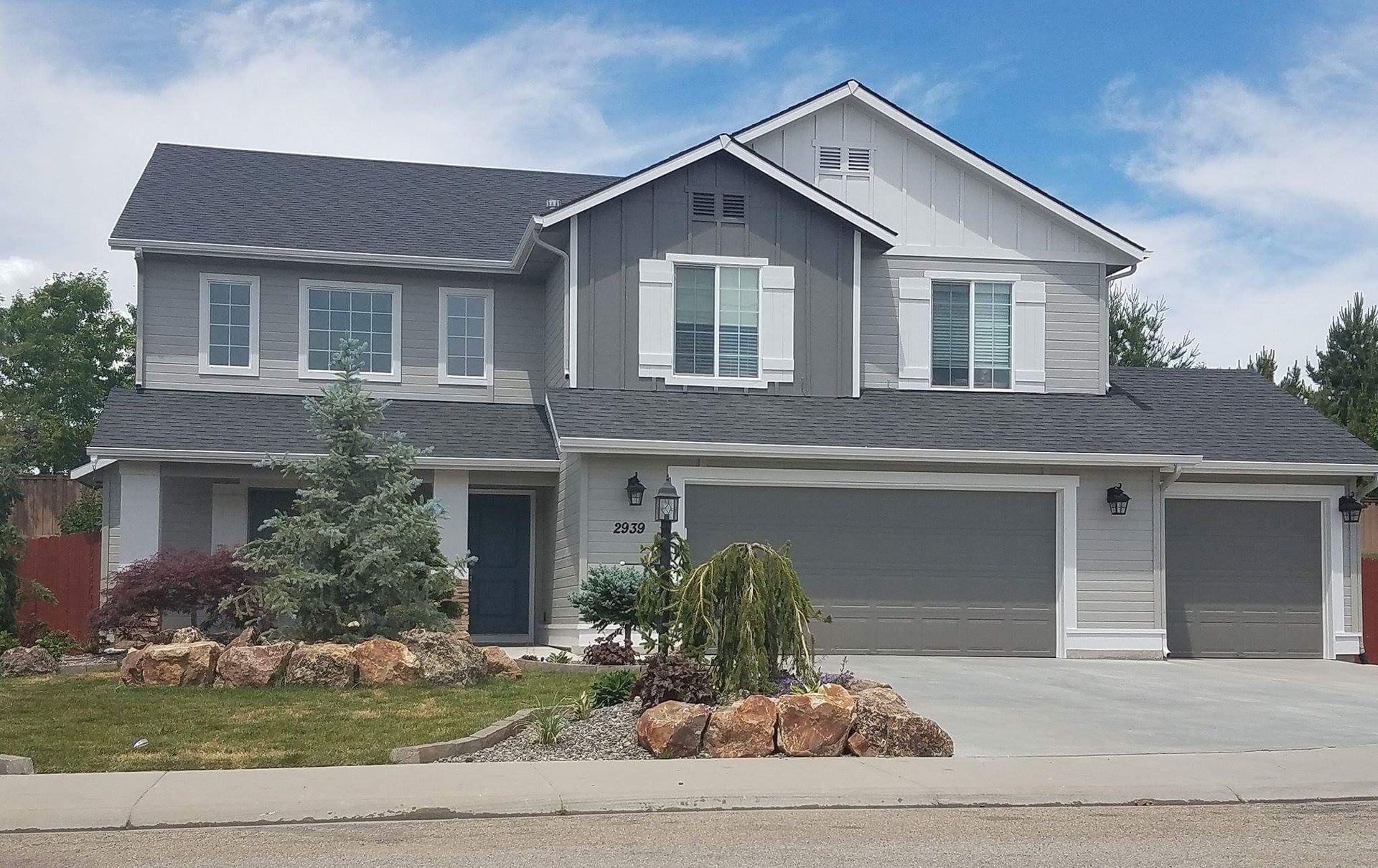 Two-story gray house with a dark gray roof, white trim, and two garage doors; set on a well-landscaped lot.