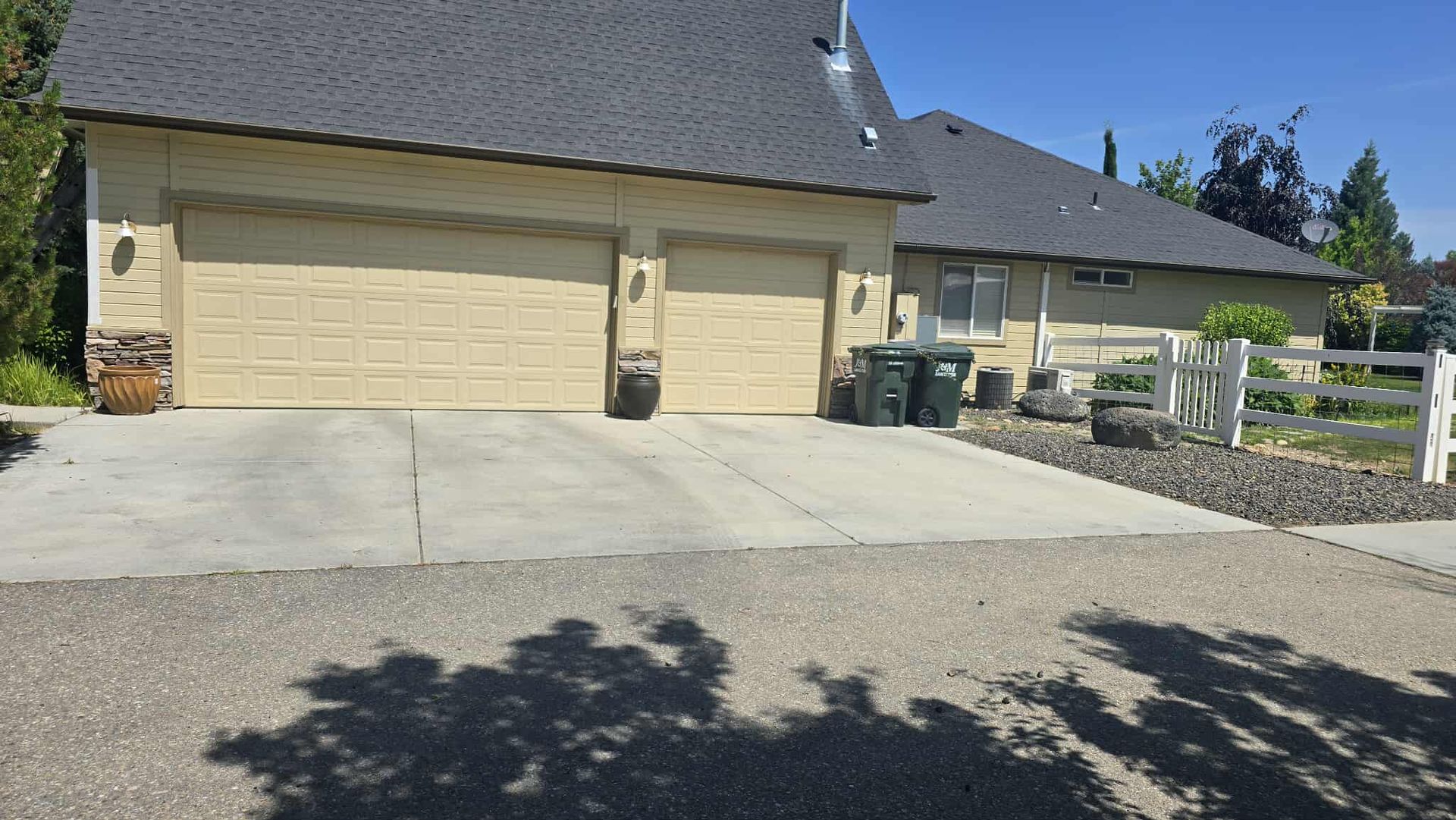 A beige garage with two doors, a concrete driveway, and gravel in front. The house has a dark roof and a small garden.