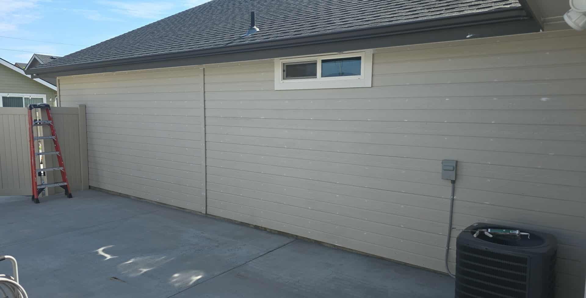 Exterior of a beige house with a concrete patio, air conditioning unit, and a ladder.