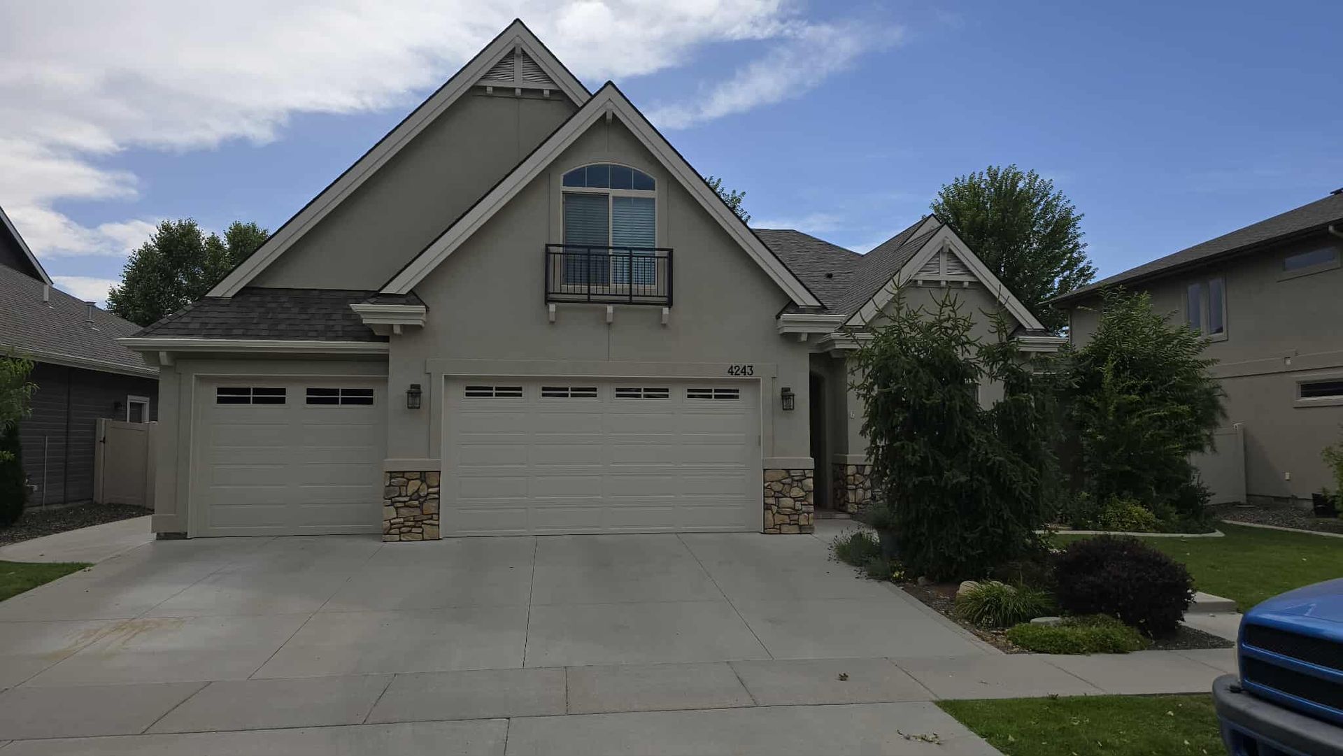 Beige house with a two-car garage, stone accents, and a small balcony under a blue sky.
