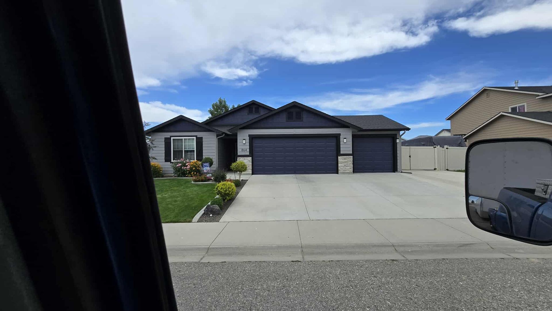 View of a house with a dark blue garage and a gray exterior, taken from inside a vehicle. A blue sky is visible.