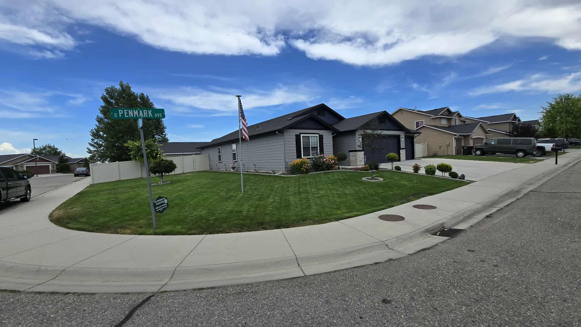 A gray house on a corner lot with green grass and a flag; a street sign reads 