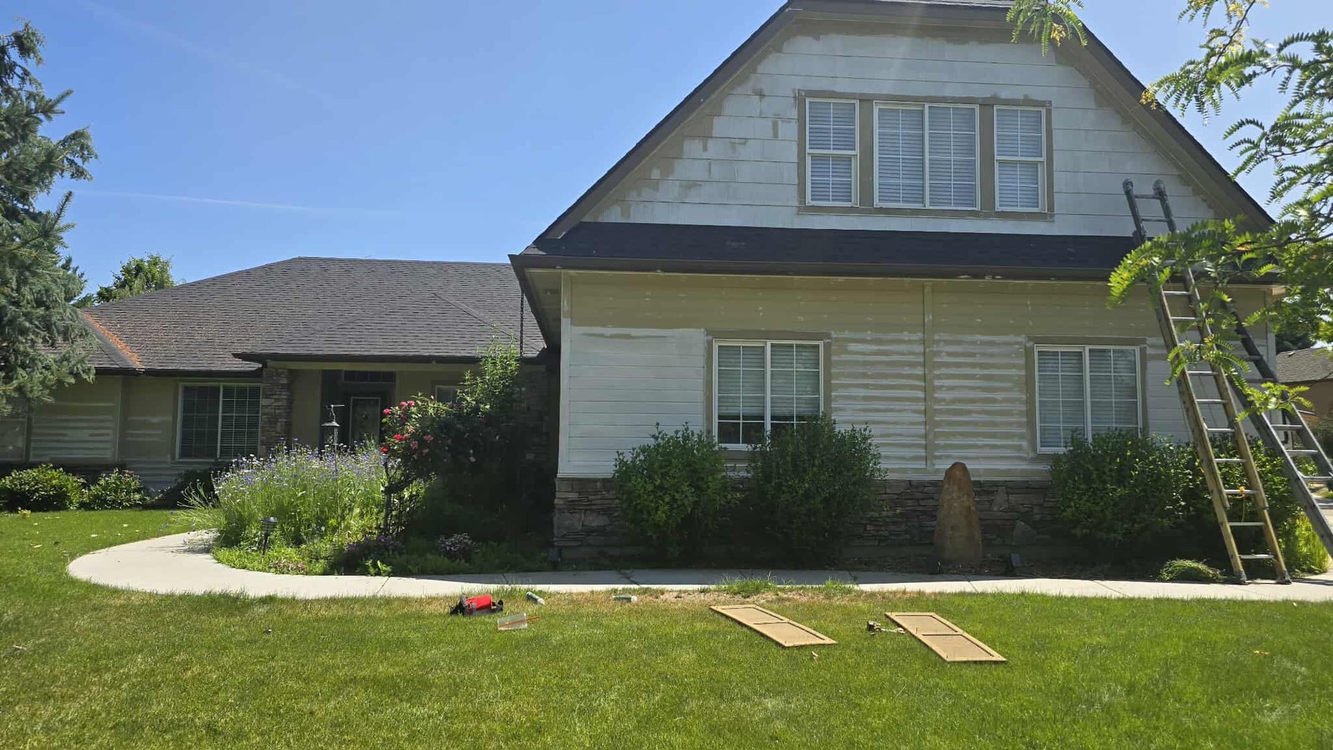 A two-story house with peeling paint, surrounded by grass and a pathway. A ladder leans against the building.