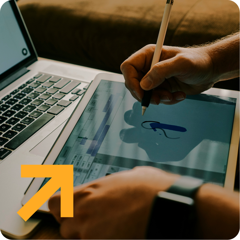 A person is drawing on a tablet in front of a laptop