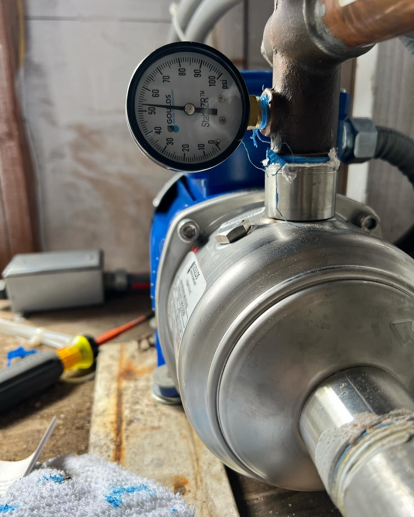 A close-up of a blue electric water pump with an attached pressure gauge, sitting on a surface with a screwdriver nearby.