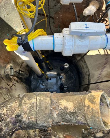 A sump pump sits in a concrete basin, connected to white PVC plumbing with a blue-labeled shut-off valve.