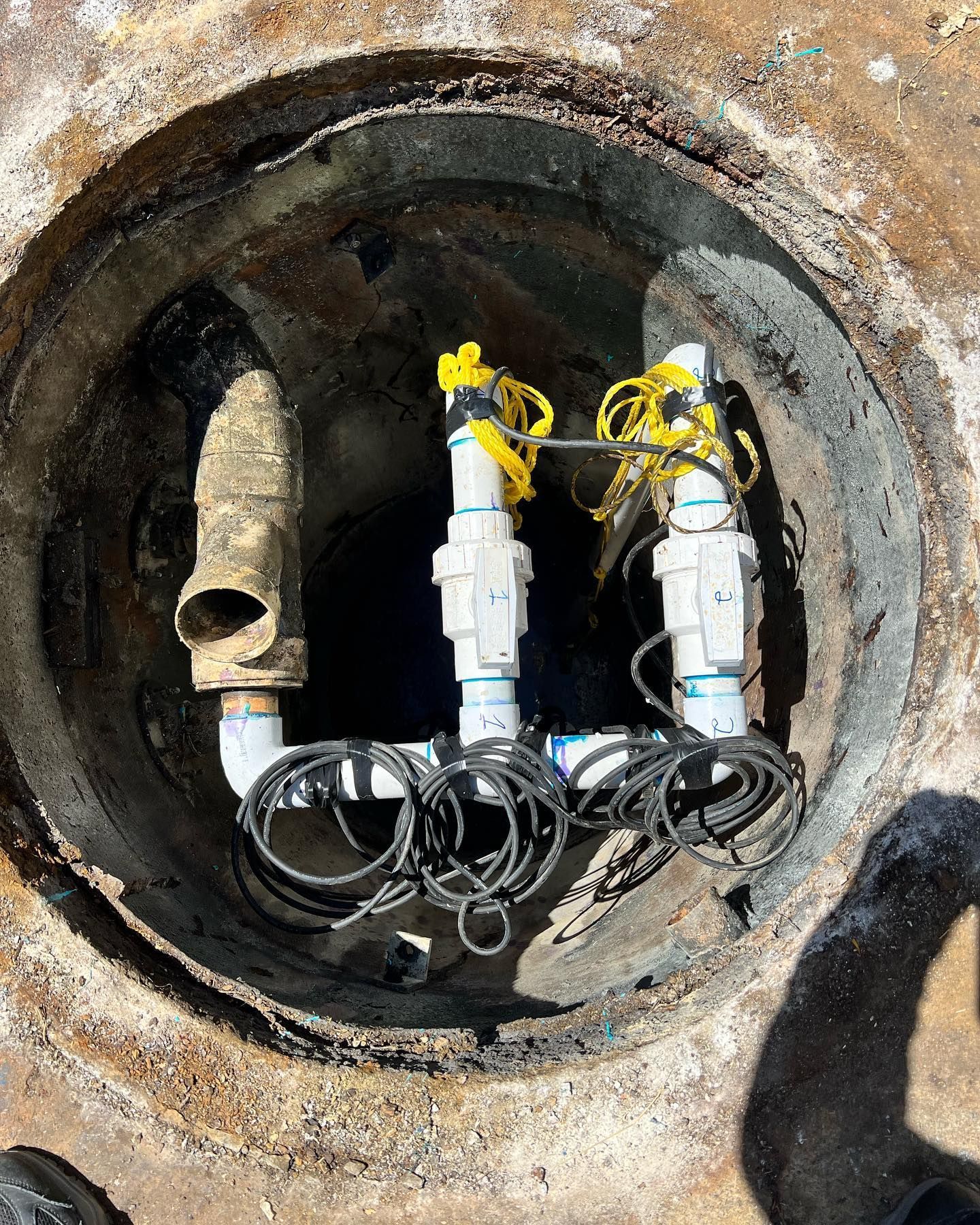 Interior of a circular utility manhole showing two white PVC pipes with black wiring and yellow tags.