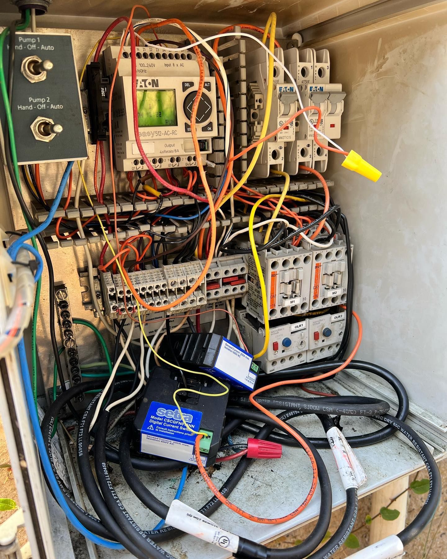 An open industrial electrical control panel with various wiring, switches, relays, and components mounted inside a box.