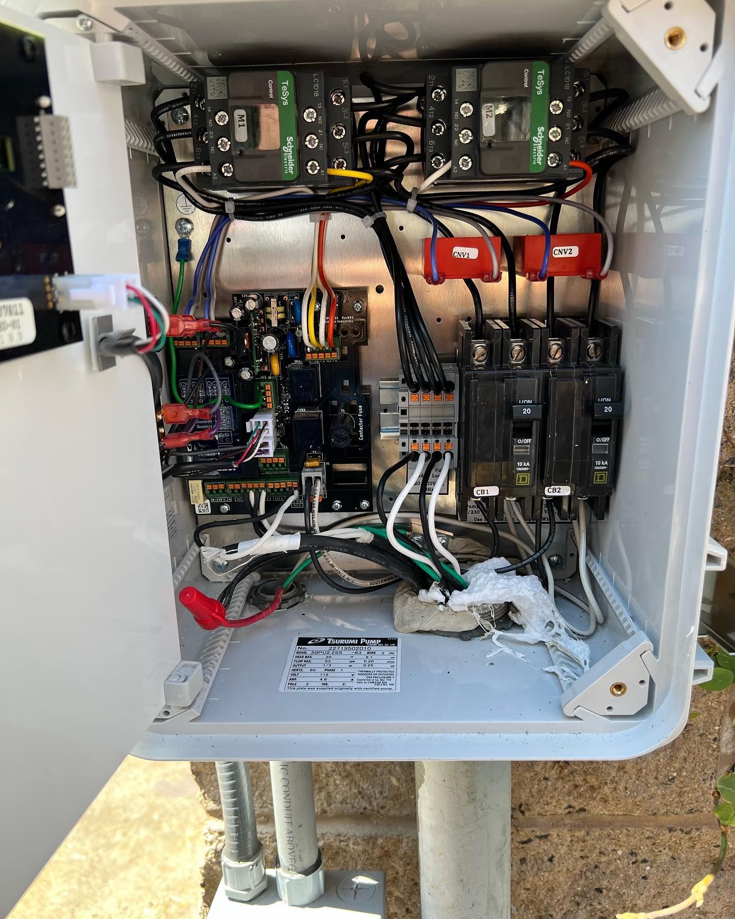 Open outdoor electrical control box mounted on a wall, showing interior wiring, circuit breakers, and relays.