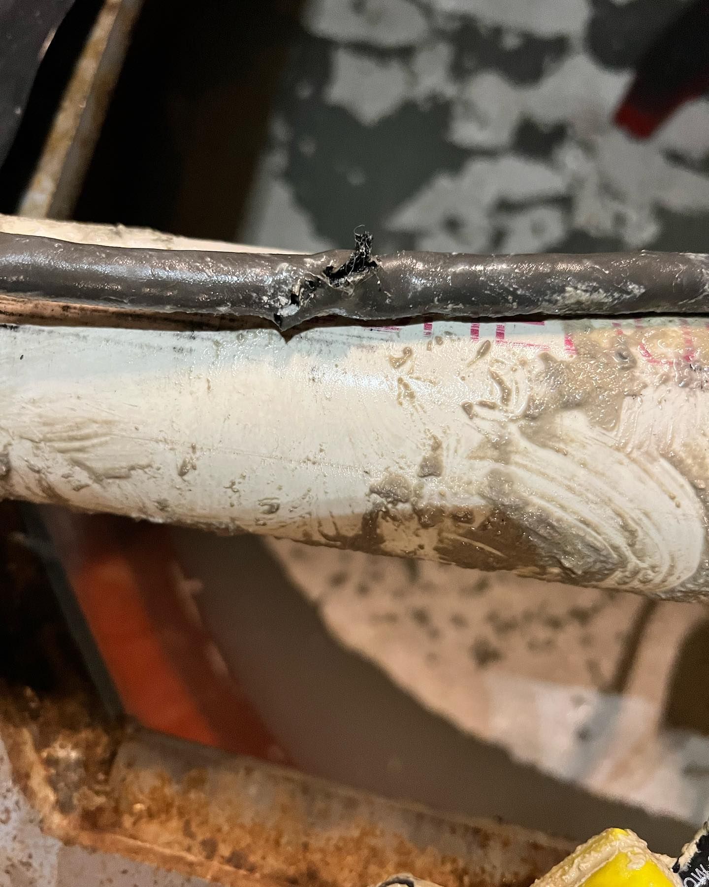 A close-up view of a metal screw piercing through a black cable that is resting on a white, dirty PVC pipe.