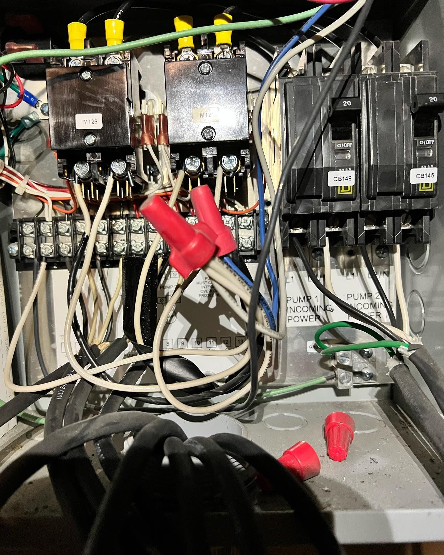Open electrical panel with two contactors, two circuit breakers, wiring, and red wire nuts connected to metal housing.
