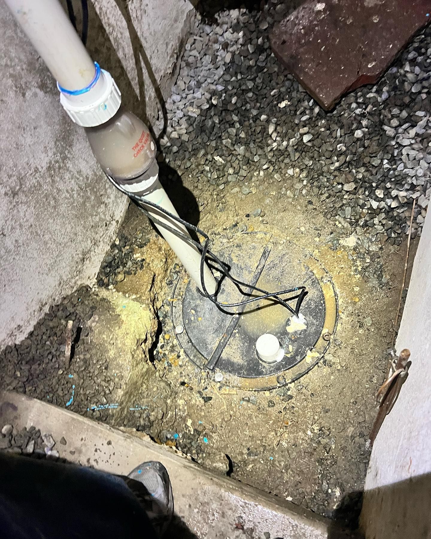A sump pump installed in a dirt-filled pit with a white discharge pipe and black power cords visible.