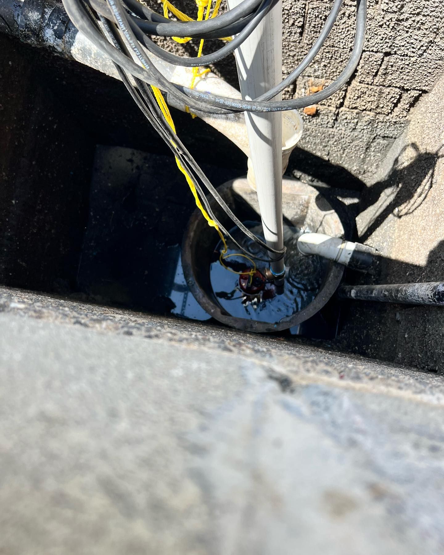 A submersible pump inside a concrete sump pit, with electrical cords coiled above and PVC piping leading out.