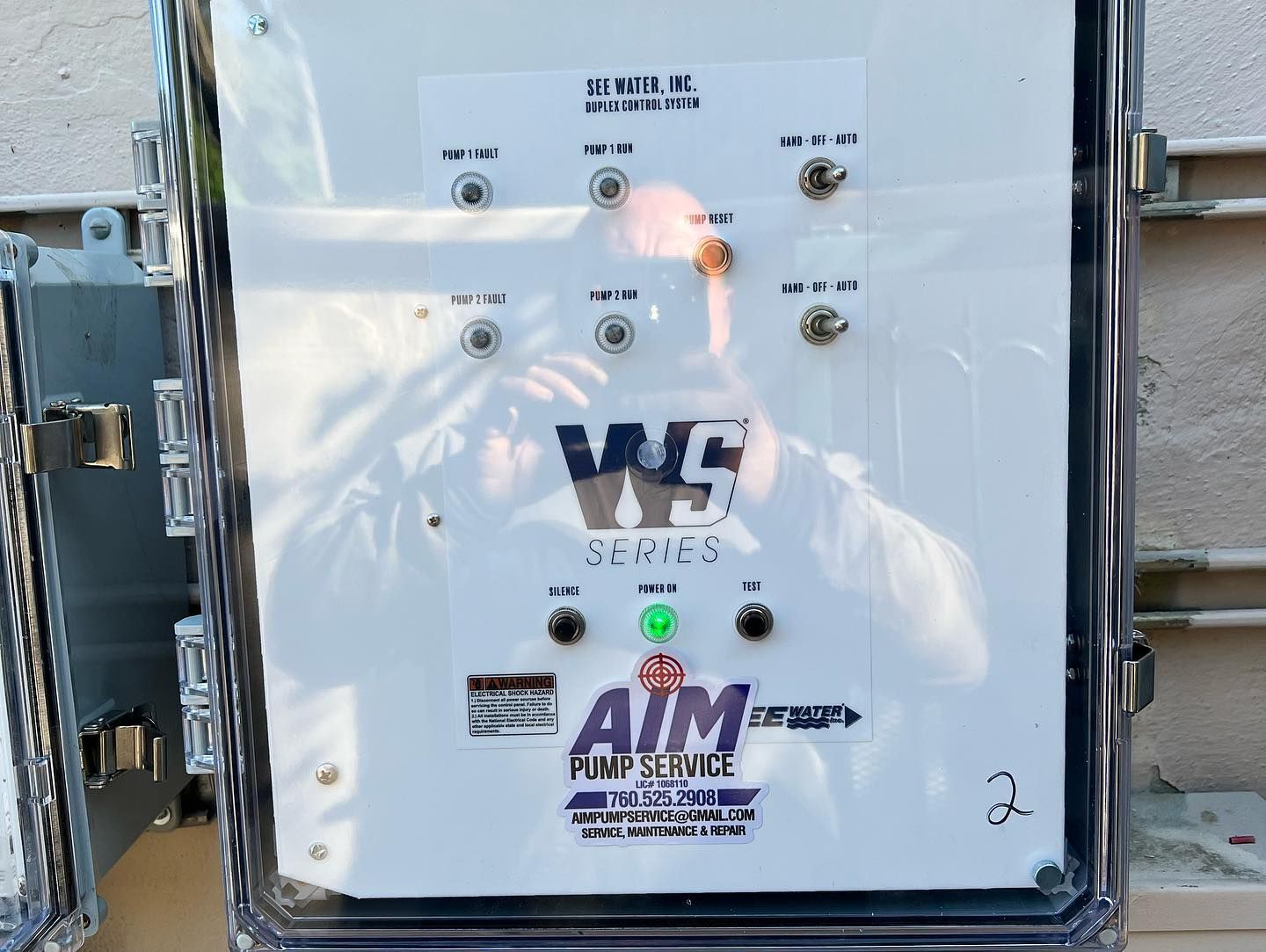 A white electrical control panel with various toggle switches, labels, and a green power light, branded by AIM Pump Service.