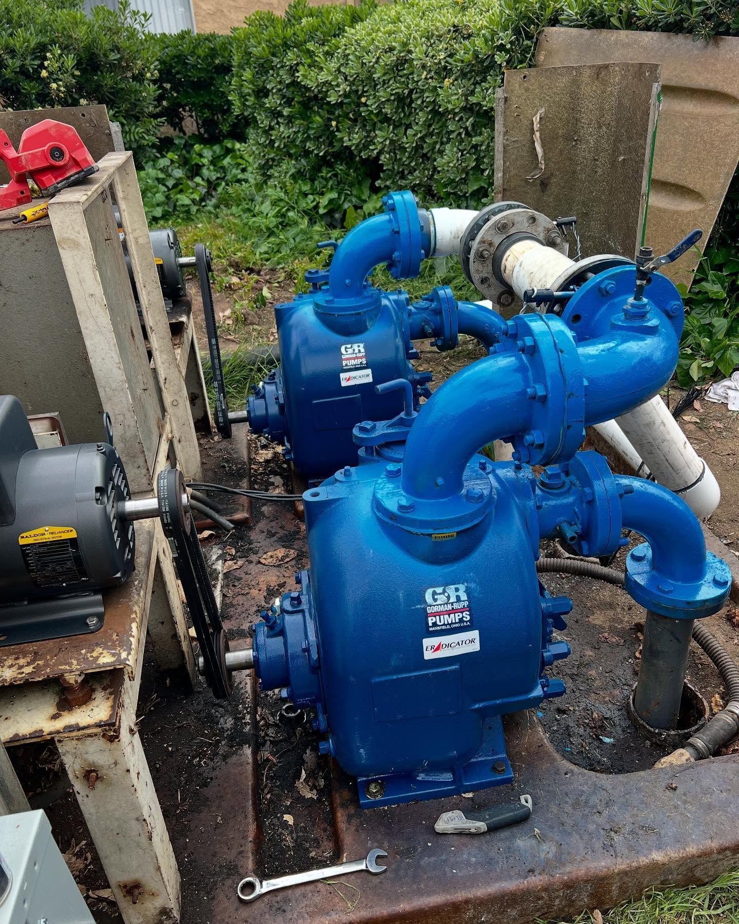 Two blue industrial pumps connected by pipes on a concrete base with an electric motor nearby.
