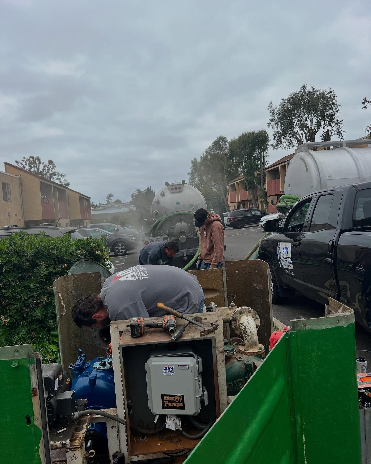 Workers inspect machinery and water tanks at a residential property on an overcast day.